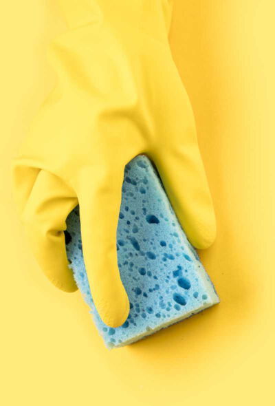 Gelber Handschuh auf gelben Hintergrund hält ein Wischmopp bei einer hygienischen Reinigung in einer Arztpraxis im Frankfurt-Rhein-Main-Gebiet. Der Gummi-Handschuh schützt die Hand vor Chemikalien einer Reinigungskraft des Reinigungsservices aus Maintal.